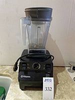 Front view of assembled Vitamix 5200C blender on countertop, showing motor base, container, lid, and tamper in background