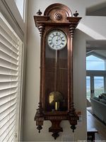 Full view of carved solid wood wall clock with glass door closed, showing upper scroll pediment and lower decorative elements