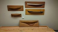 Five handcrafted wood boat hull models mounted on wall above wooden workbench