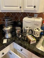 Kitchen counter with Sanyo bread machine, three Bialetti Mukka Express coffee makers, a multi-tier digital food steamer, and other kitchen items.