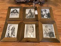 Six framed black and white photos of Native Americans arranged on the floor, showing matching rustic wooden frames; one frame corner is visibly damaged.