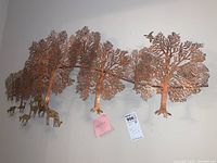 Frontal view of large metallic 3D wall sculpture showing the interconnected coppery trees and small animal figures along the bottom edge.