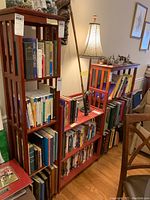 Photo of multiple wooden shelves filled with a large assortment of books covering various genres and subjects. Also includes some decorative lamps and items on top of shelves.