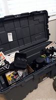 Open black storage tote containing multiple cameras, cases, and accessories placed on the floor.