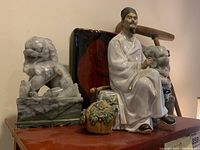 Overview of lot: marble lion bookends, ceramic figurine seated man, black and red plastic decorative piece.