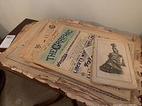 Stack of old newspapers and printed ephemera with visible title The Graphic 1914 on top, pages are yellowed and worn.