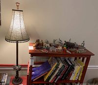 Photo showing entire lamp with animal print shade and monkey figure on base, with a collection of various souvenir figurines arranged on a wooden table next to bookshelf with books.