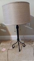 Full view of the floor lamp showing beige linen shade and black metal tripod base on carpeted floor.