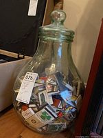 Full view of large clear decorative glass jar filled with assorted matchbooks and seller tag attached