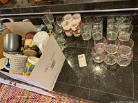 Overview photo showing a variety of mugs in a box and multiple glasses arranged on a countertop including octagon shaped glassware and clear glasses.