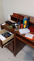 View of wooden desk with two wooden business card holders, pens, pads of paper, two large flashlights, calculator, stapler, tape dispenser, clear organizer and other small items placed on desktop.