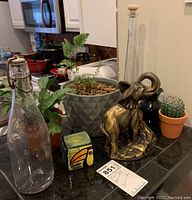 Wide shot showing all items on countertop including plants, small cactus, Costa Rica candle, elephant bookend, tall glass bottles.