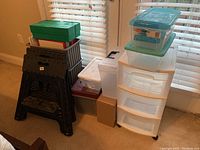 Overview of lot including plastic folding steps, wheeled storage drawers, plastic storage bins and a US Mint box.
