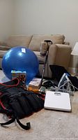 Overview of the lot showing weighted vest, blue exercise ball, body ball, cane, grippers, heating pad, and white analog bathroom scale