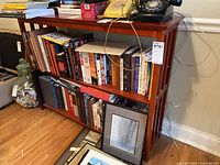 Front view of wooden shelf with slatted design, currently filled with books and framed pictures (not included in sale)