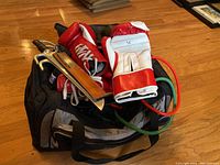 Sports equipment including boxing gloves, practice blades, lifting belt, resistance bands, all in a sports bag
