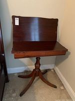Front view of wooden table against wall showing foldable and rotatable top with scalloped edges and pedestal base with claw feet.