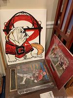 Georgia Bulldog canvas painting showing a sitting bulldog in a red jersey with a large letter G, next to two sealed Herschel Walker memorabilia pieces on the floor.