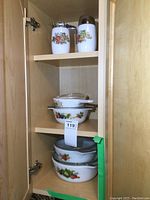 Cream and sugar set on top shelf and three casserole dishes with lids below, displaying floral and vegetable patterns.