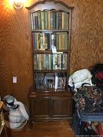 Front view of vintage wooden bookcase filled with books and DVDs on top shelves and closed cabinet below.
