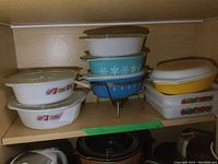 Overview photo showing stacked vintage casserole dishes of various designs including floral and solid color, with lids