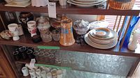 Top shelf overview showing cloisonne jars, ceramic pitcher, porcelain sugar bowl and creamer, egg cups, stacked plates and blue glass vases