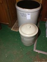 Both crocks side by side on green carpet, large 10-gallon behind small 2-gallon with lid