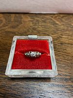 Ring on red velvet cushion in clear plastic box, top view