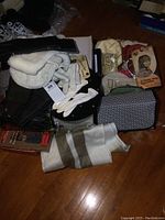 Overview photo showing a tray with several ladies clutches, wallets, gloves, a white toque, and a striped scarf on the wooden floor.