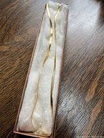 Full view of herringbone chain inside white cushioning of a long jewelry box on wood surface