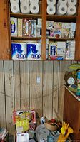 Photo of the cabinet shelf filled with multiple boxes of facial tissues, toilet paper rolls, and toiletry items.