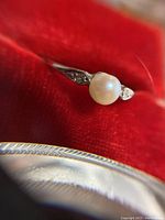 Close-up of ring showing round white cultured pearl center and single cut diamond accents in band