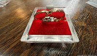 Two gold rings displayed in clear plastic stand on red velvet pad