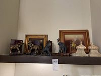 Full shelf view showing three sets of elephant bookends and ceramic decorative art, with framed artworks in the background.