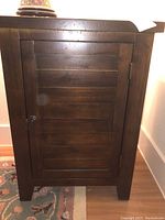 Front view of the wooden cabinet showing paneled door and metal handle.