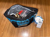 Photo showing a black and blue patterned duffel bag containing various costume jewelry pieces including necklaces, bracelets, and rings inside plastic bags.