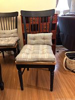 Front view of a chair showing oak-tone seat, black frame, tufted striped cushion and gingham lumbar pillow