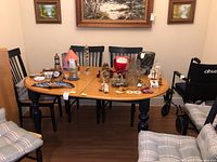 Full view of oak toned wood dining table surrounded by chairs in room, with various small items on tabletop.