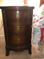 Photo of vintage Sheridan style nightstand with three curved drawers and ornate oval brass pulls in dark wood finish.