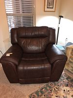 Full front view of brown leather recliner chair on carpet, showing cushioned armrests and padded backrest.