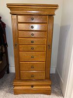 Front view of the oak jewelry chest showing all 9 drawers with round metal knobs and side vertical fluted accents.