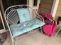 White metal outdoor loveseat with blue patterned seat and back cushions on a porch floor near sliding glass doors. Pink folding chaise positioned to the side.