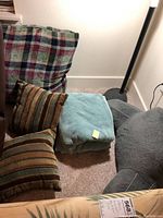 Five item lot of assorted pillows and two folded teal Columbia fleece blankets on carpeted floor