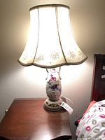 Porcelain lamp with colorful floral design visible on base, illuminated cream silk lampshade with gold floral details