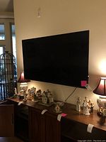 Wall-mounted 55 inch flat screen TV above a wooden cabinet with decorative figurines and lamps on each end.
