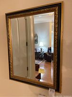 Photo of the rectangular wall mirror with dark wood frame and carved gold accent details. Beveled glass visible around the mirror edges.
