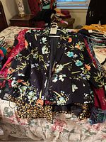 Overview showing black satin jacket with detailed floral embroidery on top of other jackets including leopard print and floral patterns