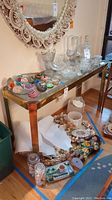 Console table shown with various glass paperweights and bowls on top, highlighting the rectangular brass frame and beveled glass top.