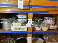 Wide shelf view of several ceramic and glass baking and serving dishes including CorningWare and floral pattern bakeware, plus large metal serving pots.