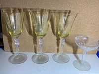 Three yellow wine glasses with clear ornate stems and one coupe champagne glass with frosted design photographed on a white surface against a brown background.
